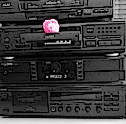 Ein haekelschwein sitzt auf der herausgefahrenen CD-Schublade eines HiFi-Turms.